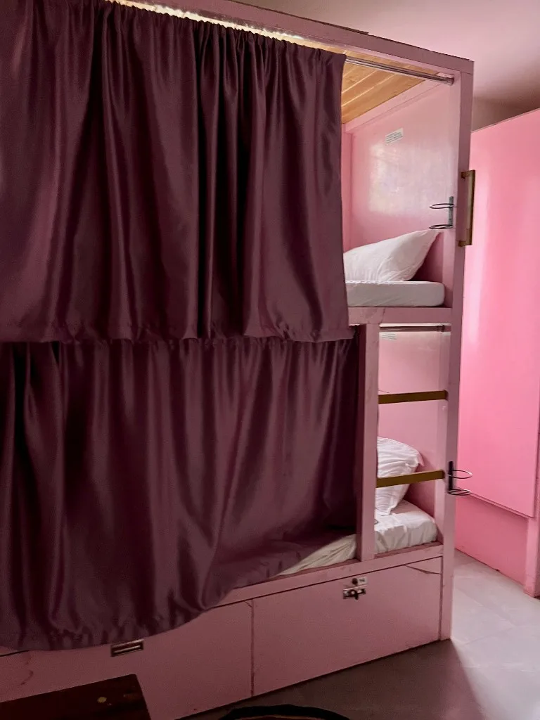 Pink bunk beds with privacy curtains and storage for budget dorm stay during 100 hour yoga teacher training Goa