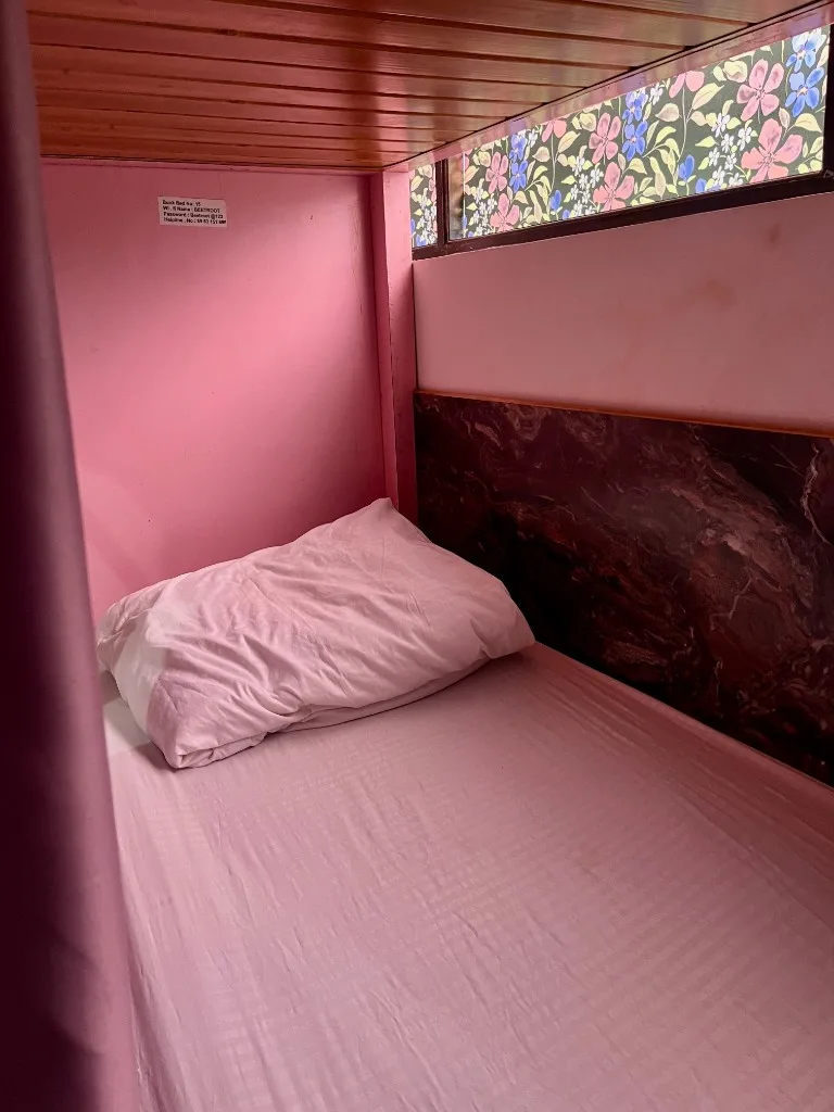 Comfortable pink-themed dorm bunk with privacy curtain for yoga teacher training accommodation in Goa