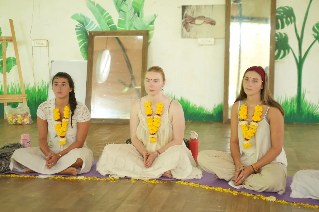 Opening ceremony seated on purple mats beside tropical leaf mural at Divinepath Goa