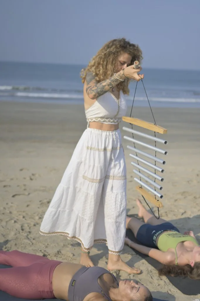 Facilitator playing bar chimes during a beach sound healing session in Goa