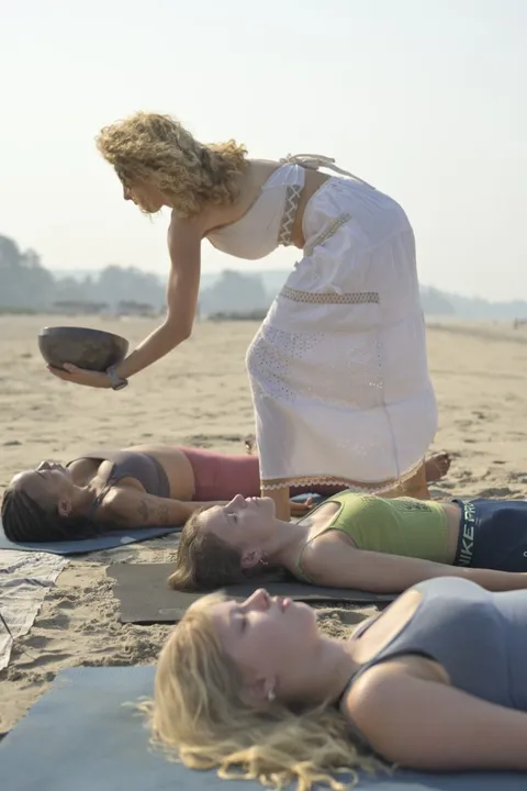Hands-on singing bowl practice over a participant on the beach