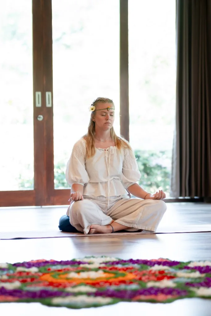 Student meditating in a Divinepath yoga shala with a flower mandala in the foreground
