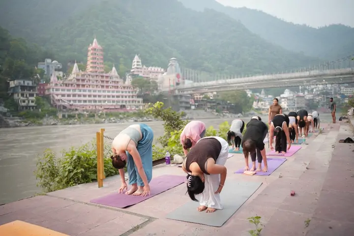 Standing forward fold on the Ganga ghat, included in 200 hour yoga teacher training Rishikesh fees