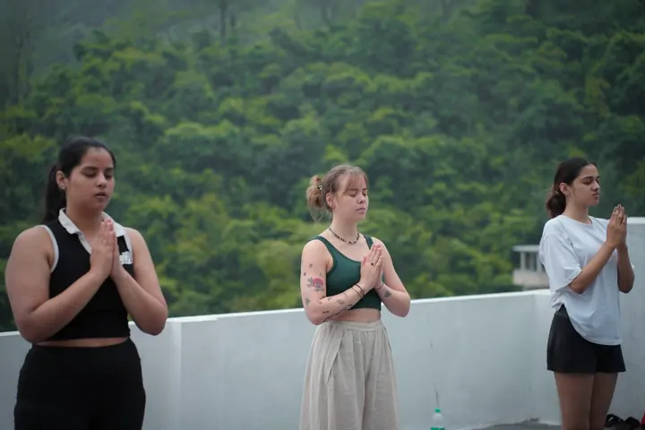 Trainees in prayer pose on the rooftop during a 200-hour yoga teacher training in Rishikesh