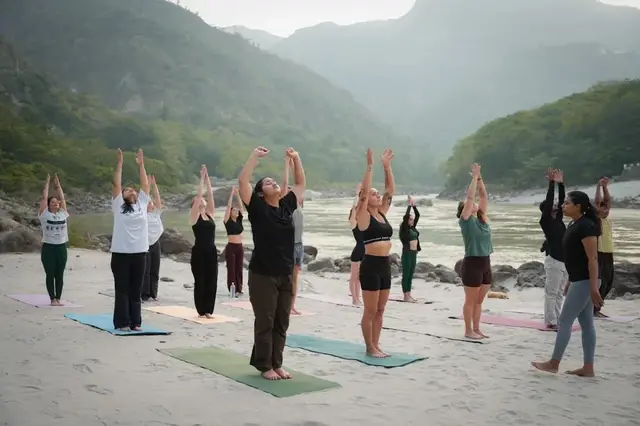 Yoga class by the Ganges with arms raised in Rishikesh