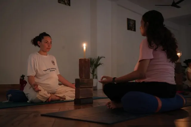 Two trainees in a candlelit prenatal yoga practicum with stacked blocks in the Tapovan hall