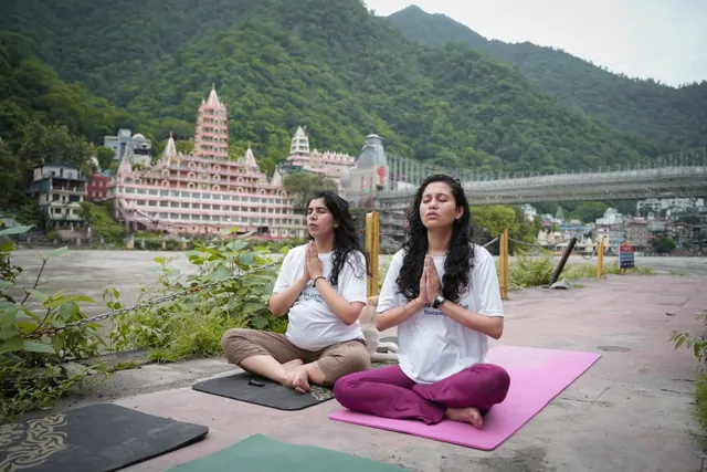 Pregnant trainee and classmate in namaste by the Ganga during in-person prenatal yoga training in Rishikesh