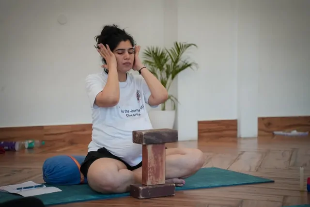 Pregnant yoga trainee using blocks for a seated pose during prenatal teacher training in Rishikesh